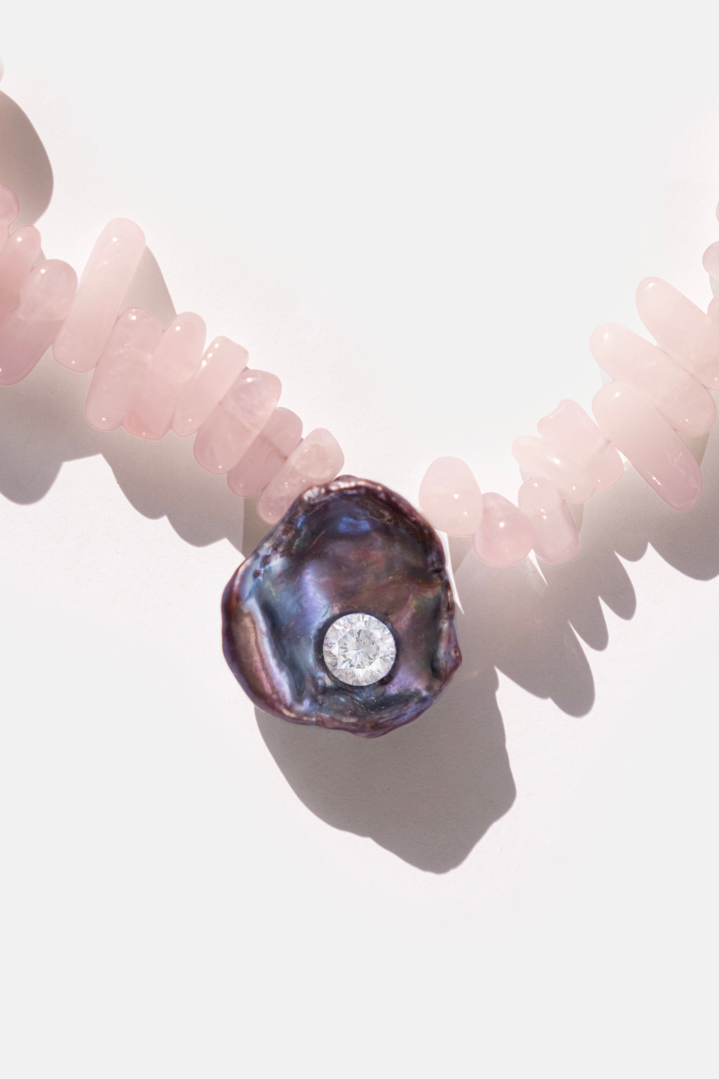 Necklace with pink quartz stones and a purple black keshi pearl and white cubic zirconia crystal gemstone on a white background