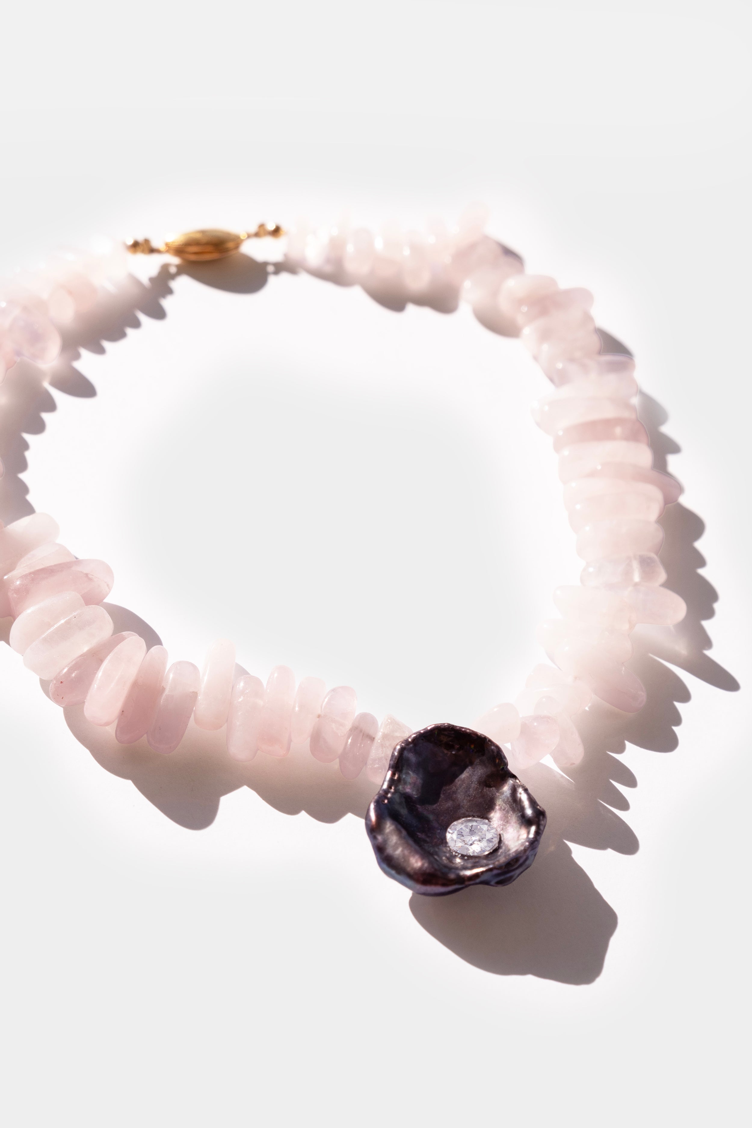 Necklace with pink quartz stones and a purple black keshi pearl and white cubic zirconia crystal gemstone on a white background