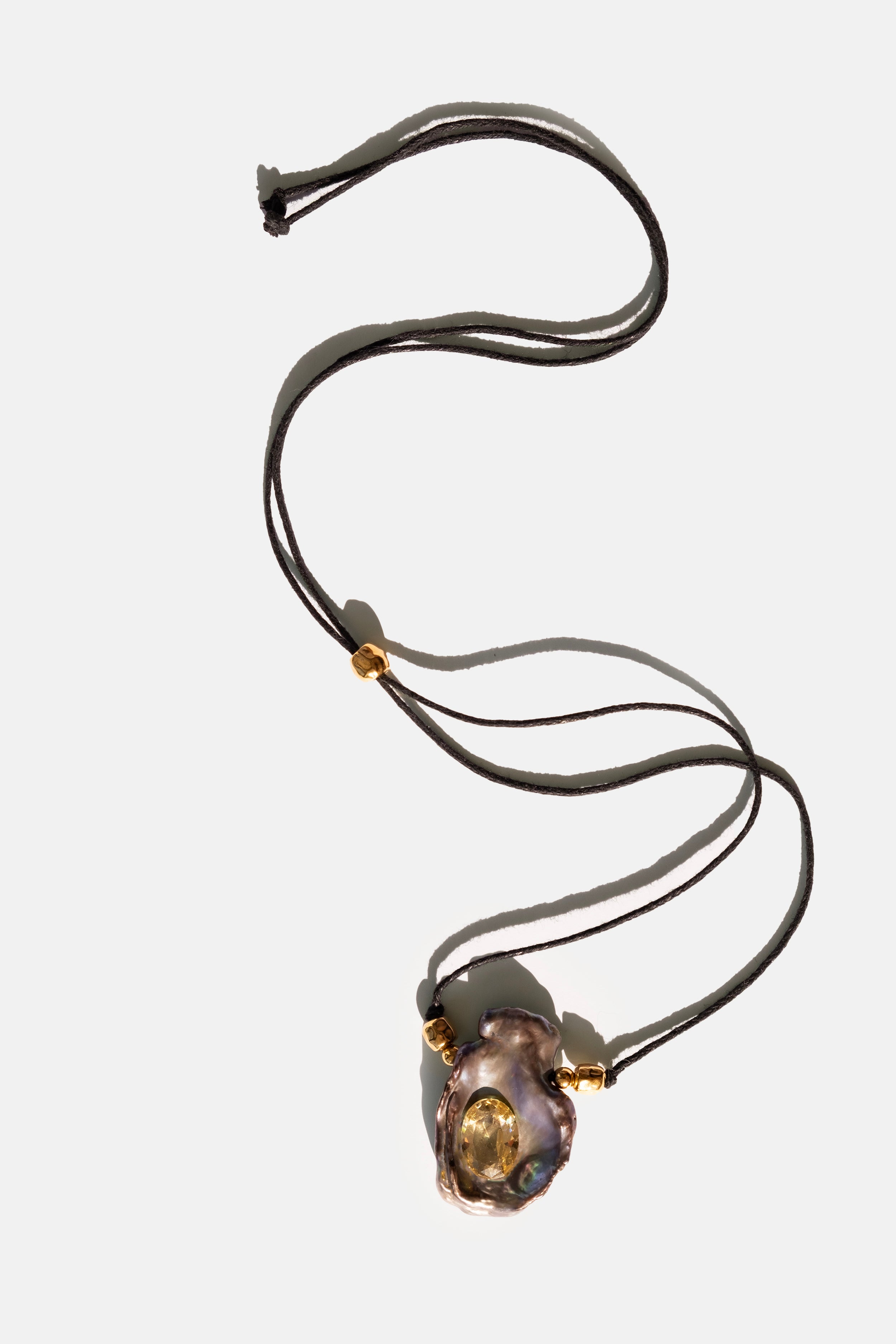 Necklace with a black keshi pearl pendant and gold crystal on a white background